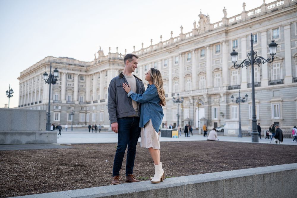 Couple sharing a romantic moment in front of the Royal Palace of Madrid on a sunny day.