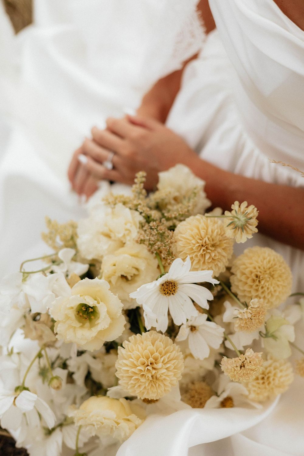 Bridal bouquet of white daisies, cream dahlias, and ivory roses held by a bride in a white wedding dress.