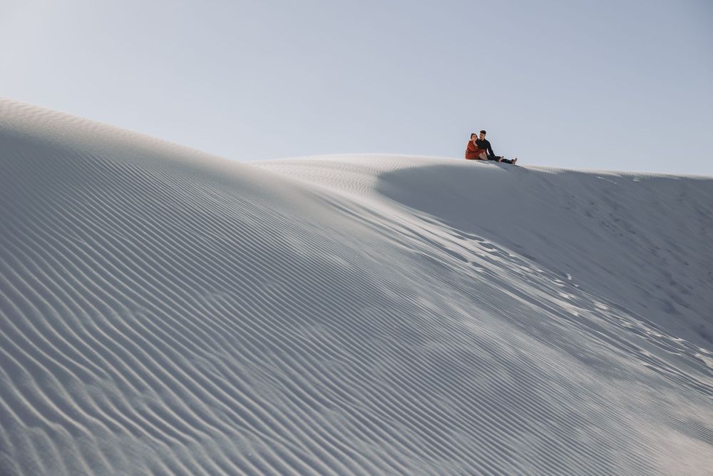 Person sitting atop a white sand dune with rippled texture under a clear sky at White Sands National Park.