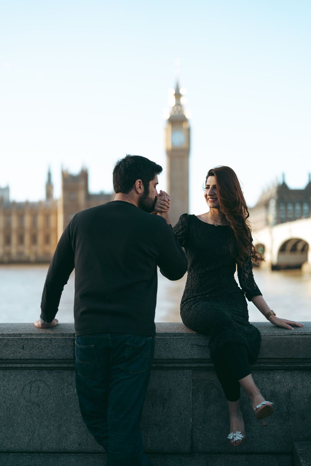 Romantic couple holding hands by the Thames River with Big Ben and Houses of Parliament in background, London.