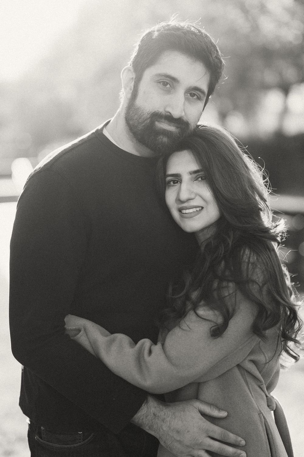 Black and white portrait of a bearded man and woman embracing tenderly outdoors.