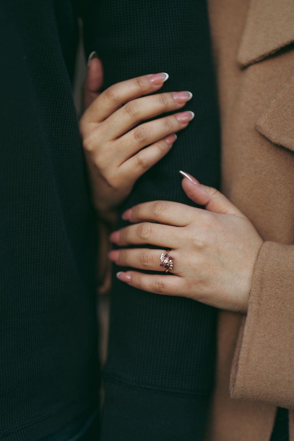 Close-up of a woman's hands with French manicure and rose gold ring gently holding a man's arm.