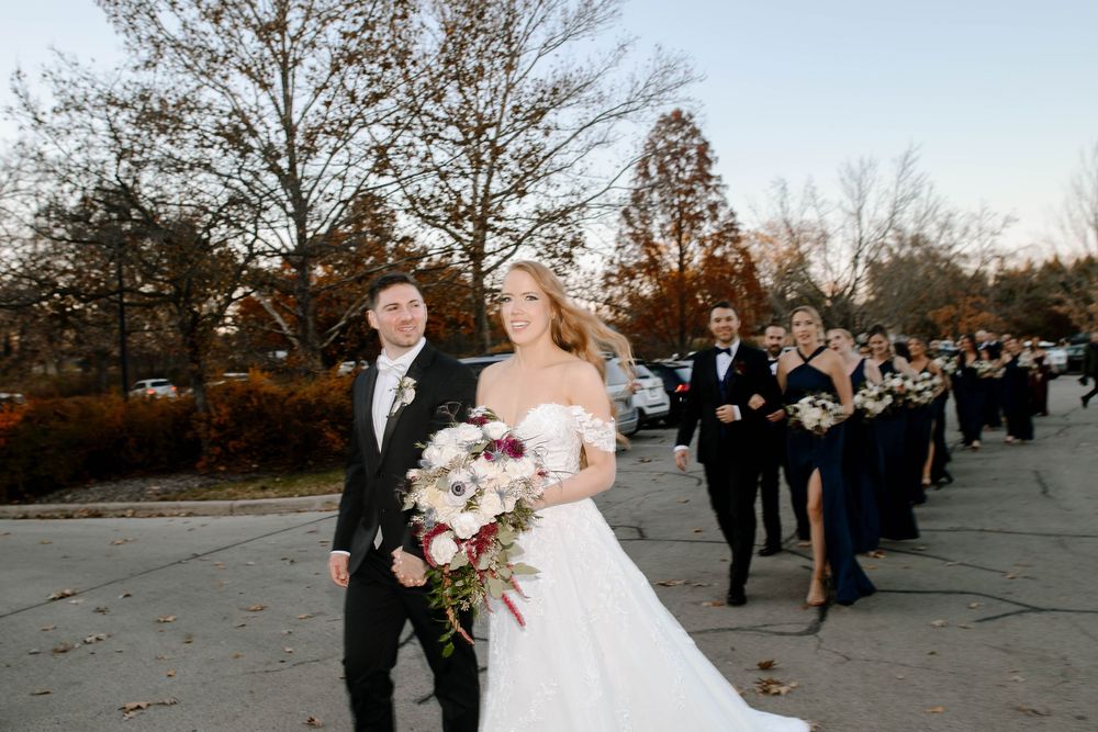 Bride and groom leading wedding party outdoors in autumn setting with bouquet.