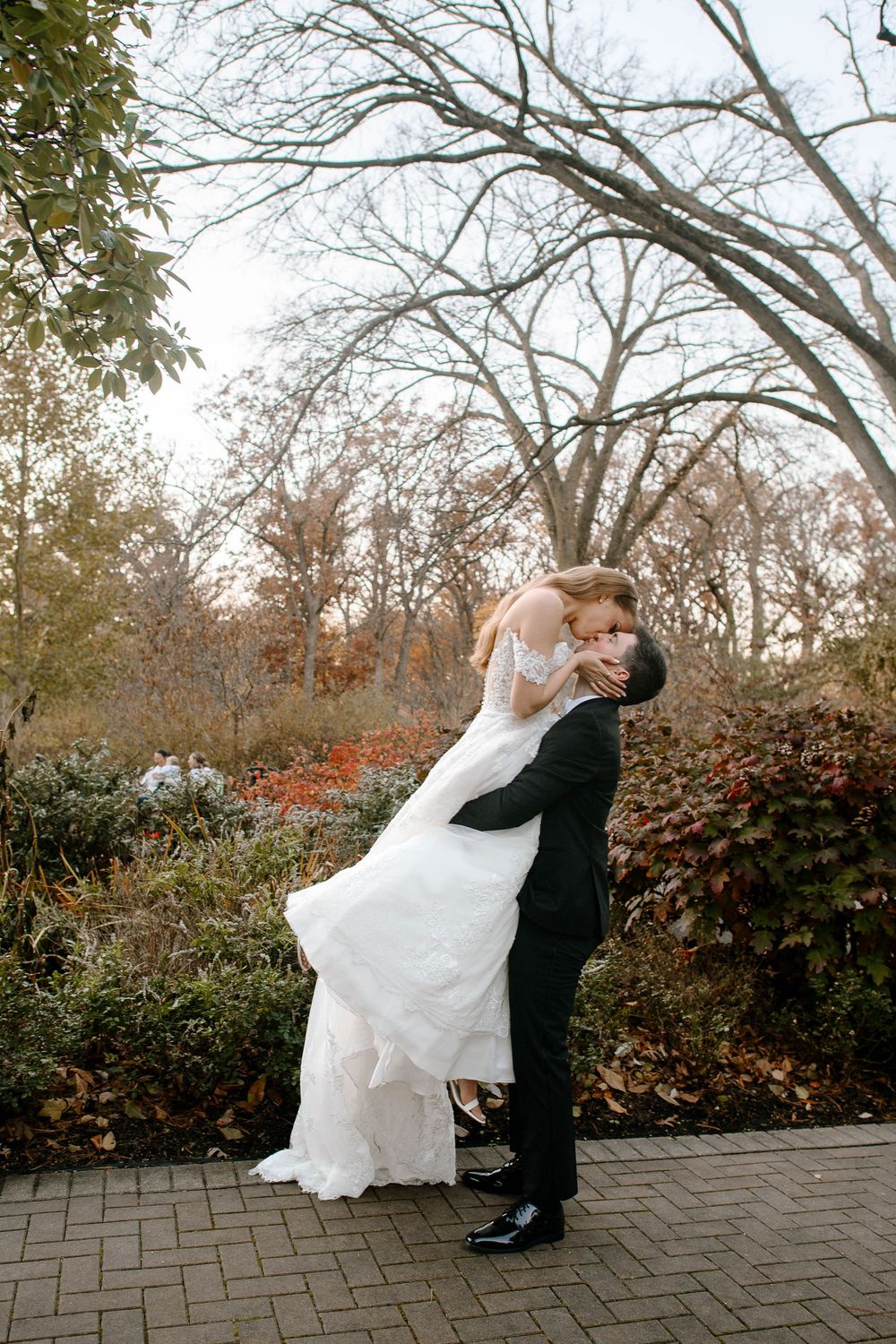 Groom lifts bride in a romantic dip kiss surrounded by autumn foliage in an outdoor wedding portrait.