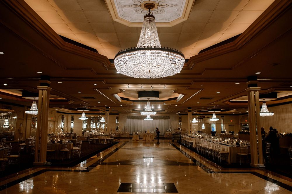 Elegant wedding reception ballroom with grand crystal chandeliers, polished marble floors, and warm ambient lighting.