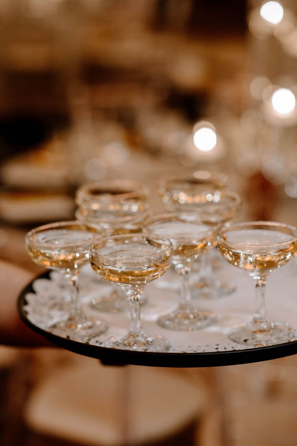 Server holding a tray of champagne coupe glasses filled with sparkling wine at a wedding reception.