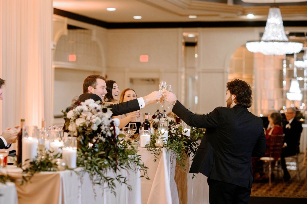 Wedding guests raising champagne glasses in a toast near a floral centerpiece at a reception.