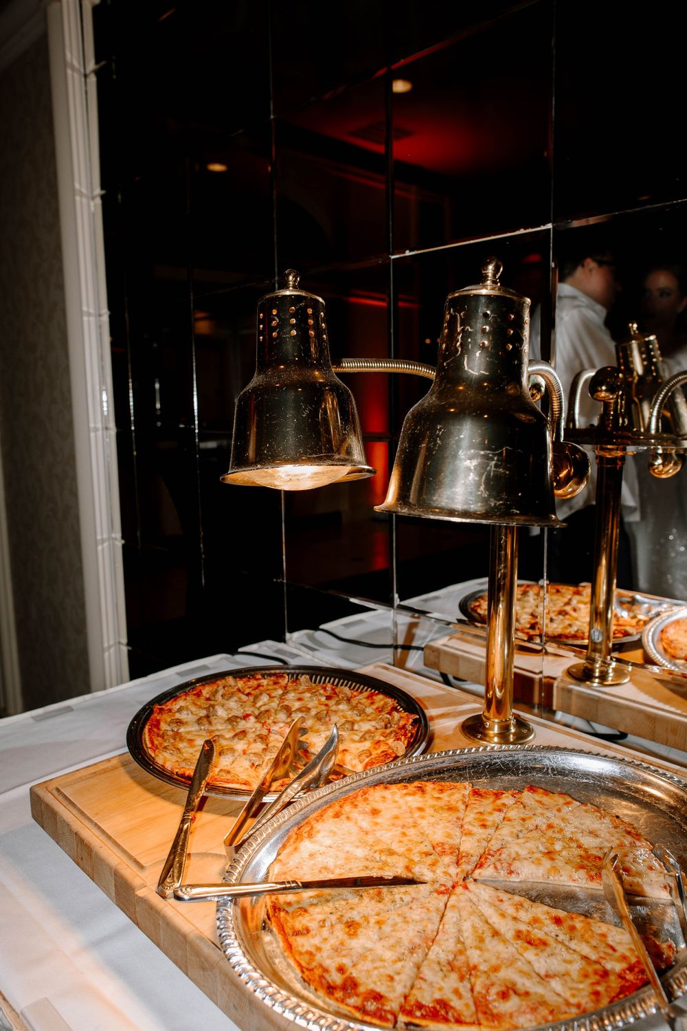 Pizza buffet station with gold heat lamps keeping sliced pizzas warm at an elegant wedding reception.