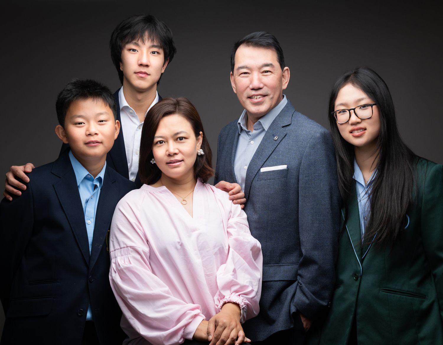 Family of five posing together for a professional portrait photo against a dark studio background.