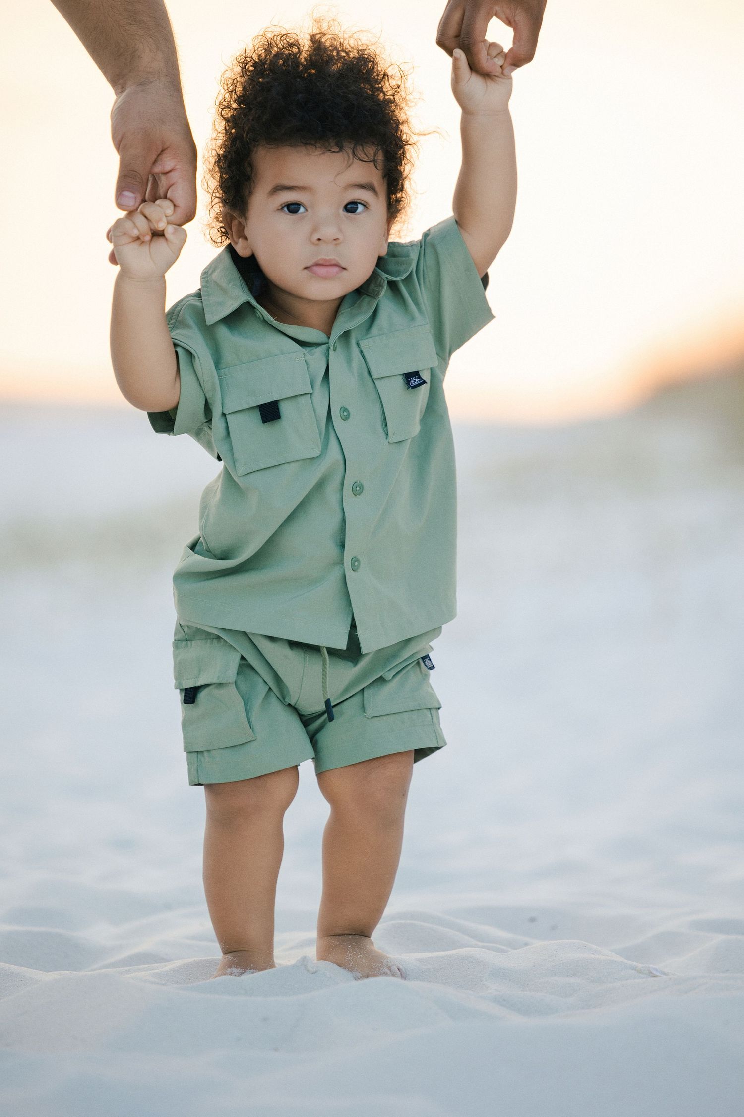 family of three holding a toddler standing on pensacola beach sand during golden hour sun