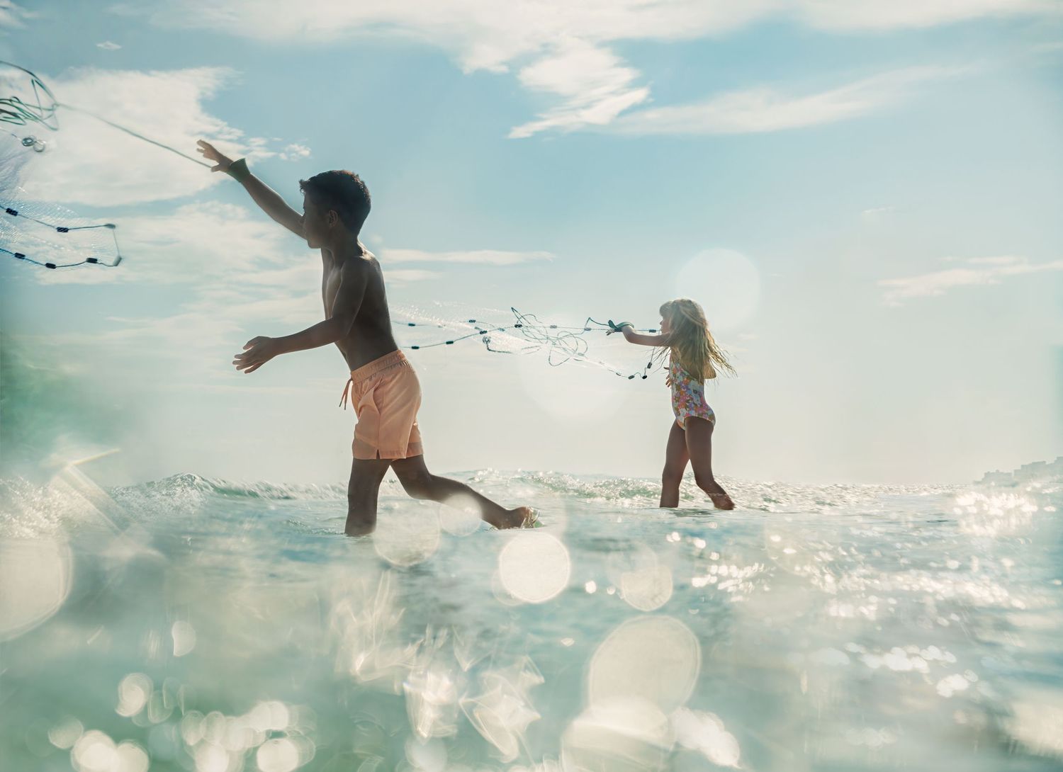 Two children play in shallow ocean waves, photographed from an underwater perspective.