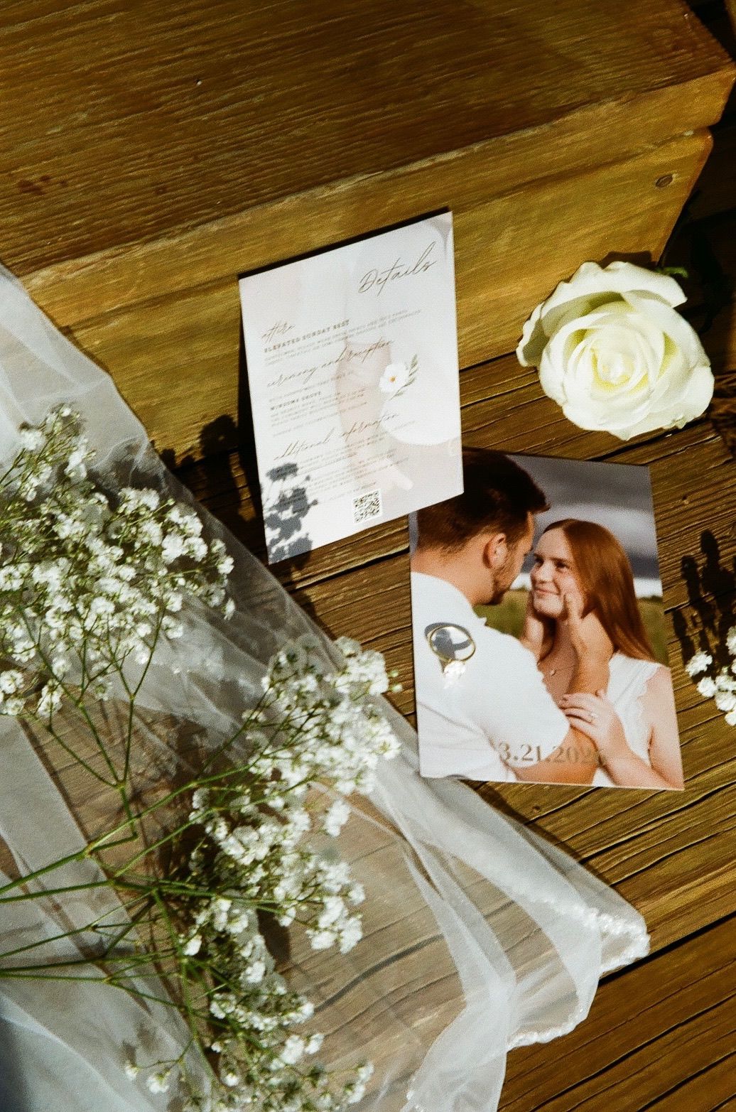 Wedding photo and invitation on wooden surface with white roses and baby's breath flowers, romantic couple portrait.
