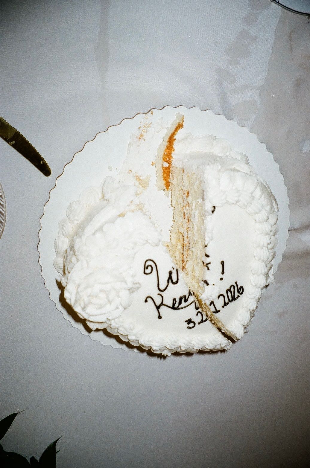Top view of a partially cut white wedding cake with Ken inscription and date 3.21.2026.