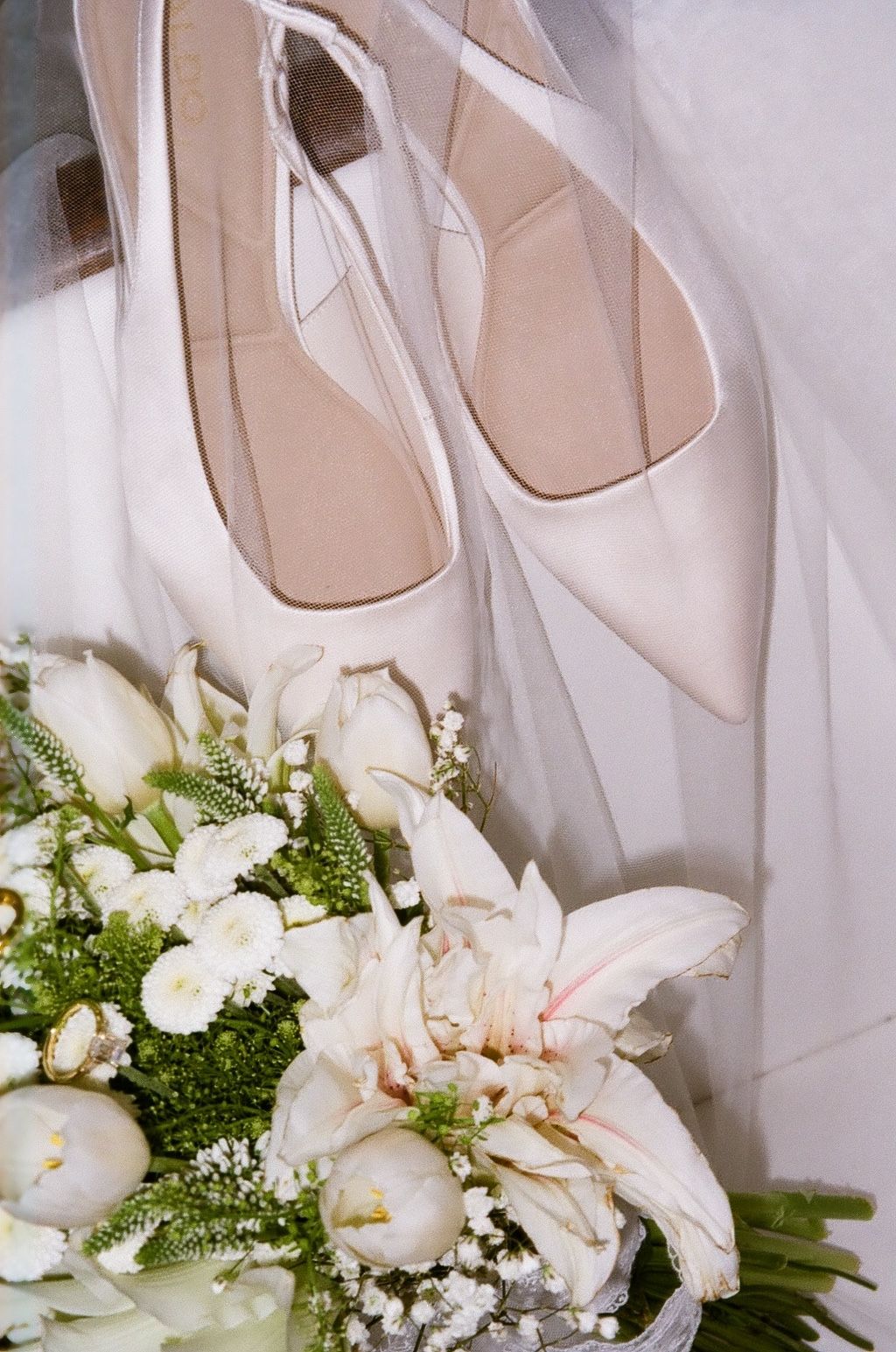Elegant nude pointed-toe bridal heels rest beside a white wedding bouquet with lilies and tulips.