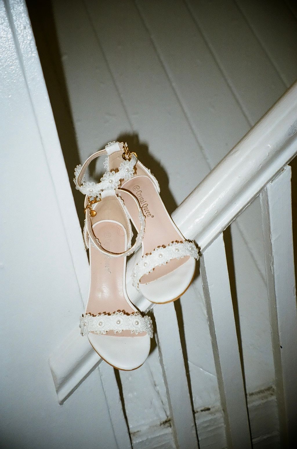 White bridal heeled sandals with pearl and floral embellishments displayed on a white staircase railing.