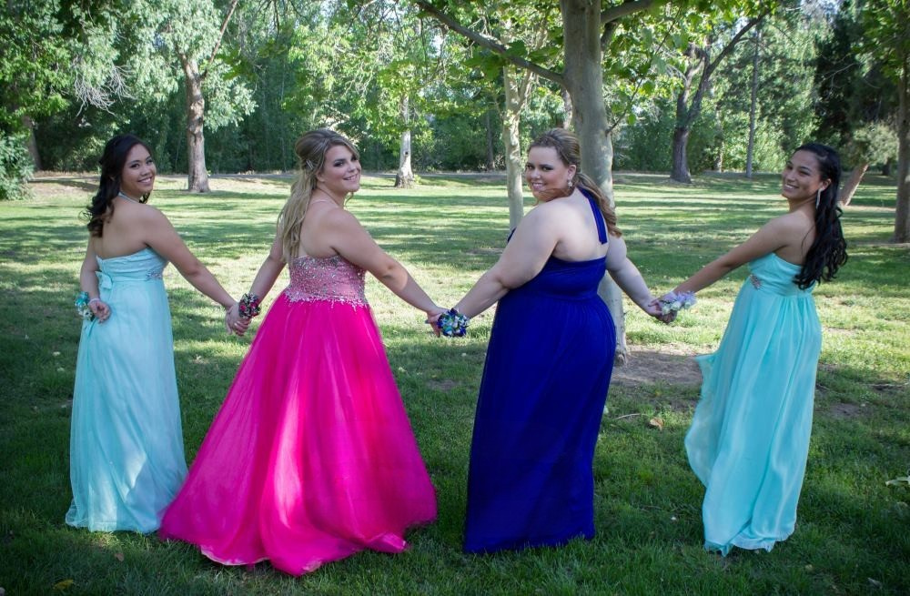 Four young women in formal gowns holding hands before the prom.