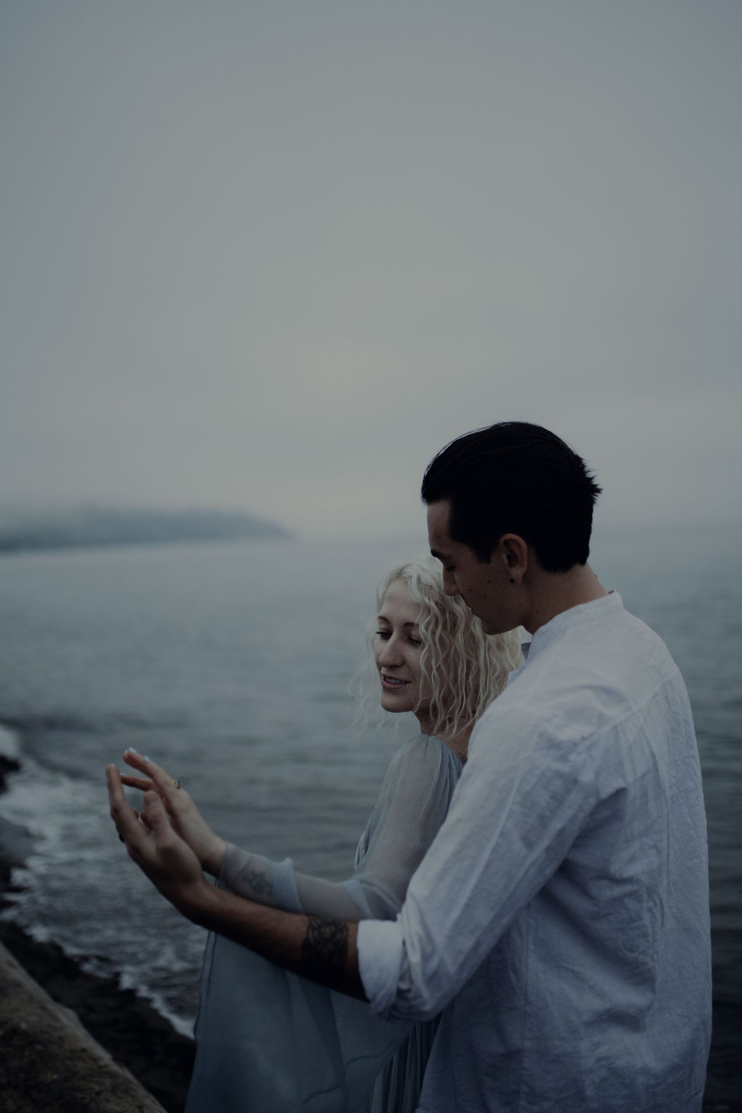A couple shares an intimate moment while dancing on a rocky beach.