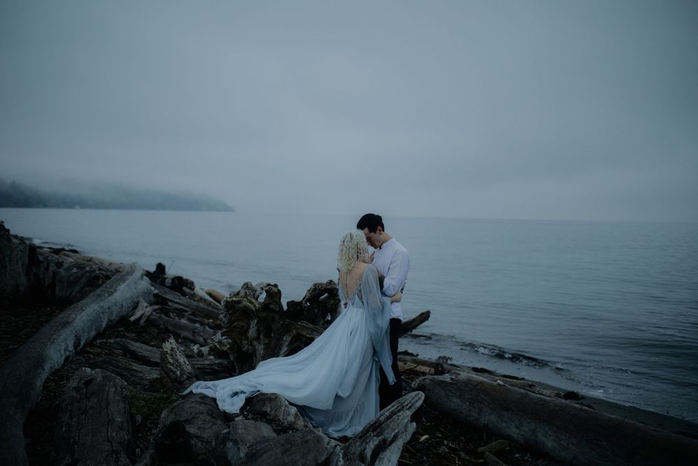 Two people share an intimate moment on rocky coastal cliffs overlooking the ocean.