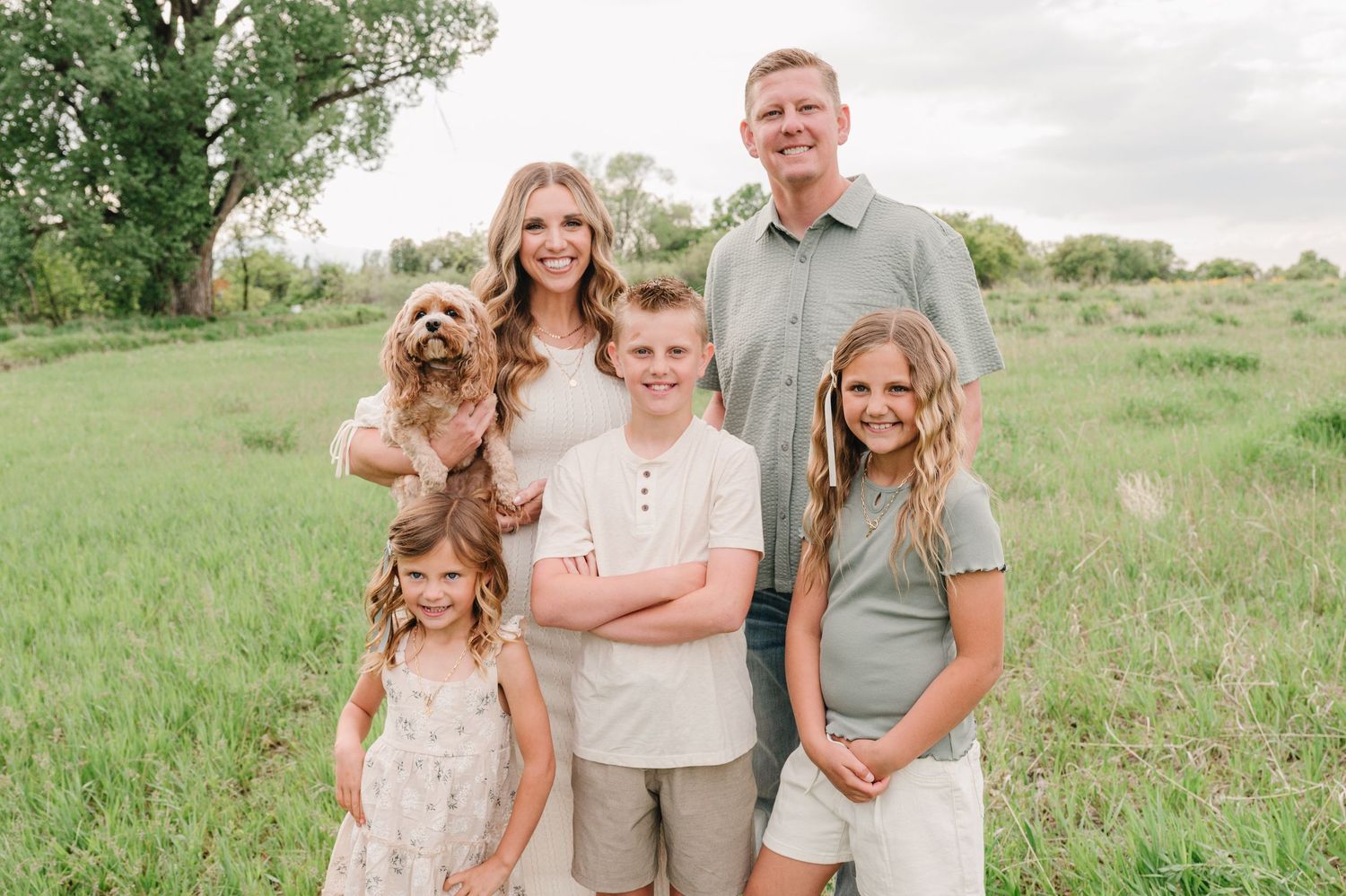 A happy family poses together with their golden retriever dog in a green meadow on a summer day.