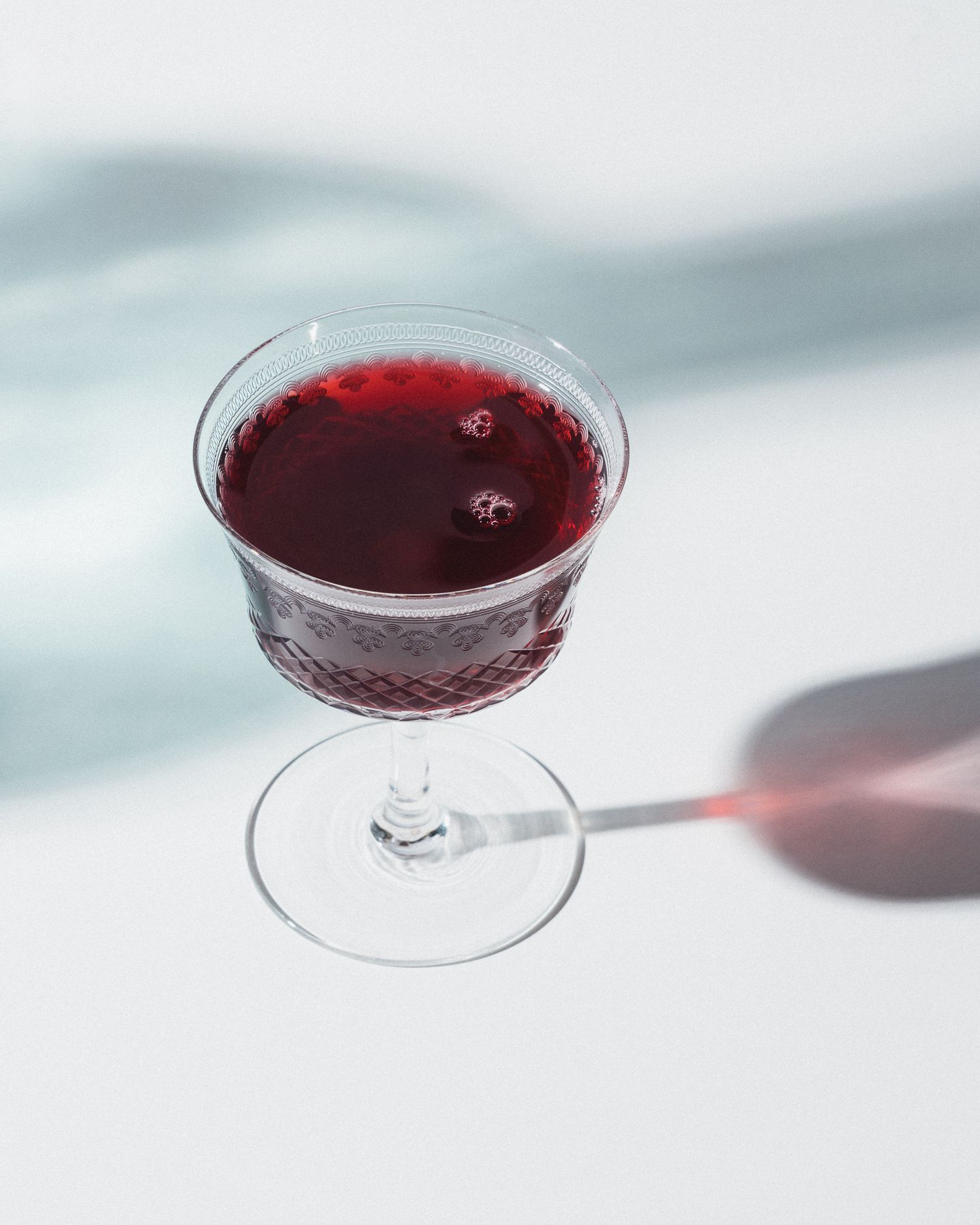 Imagefotografie für einen Bio-Beerensirup, dunkelroter Saft in einem kleinen Glas mit Stil, sonnige Lichtstimmung