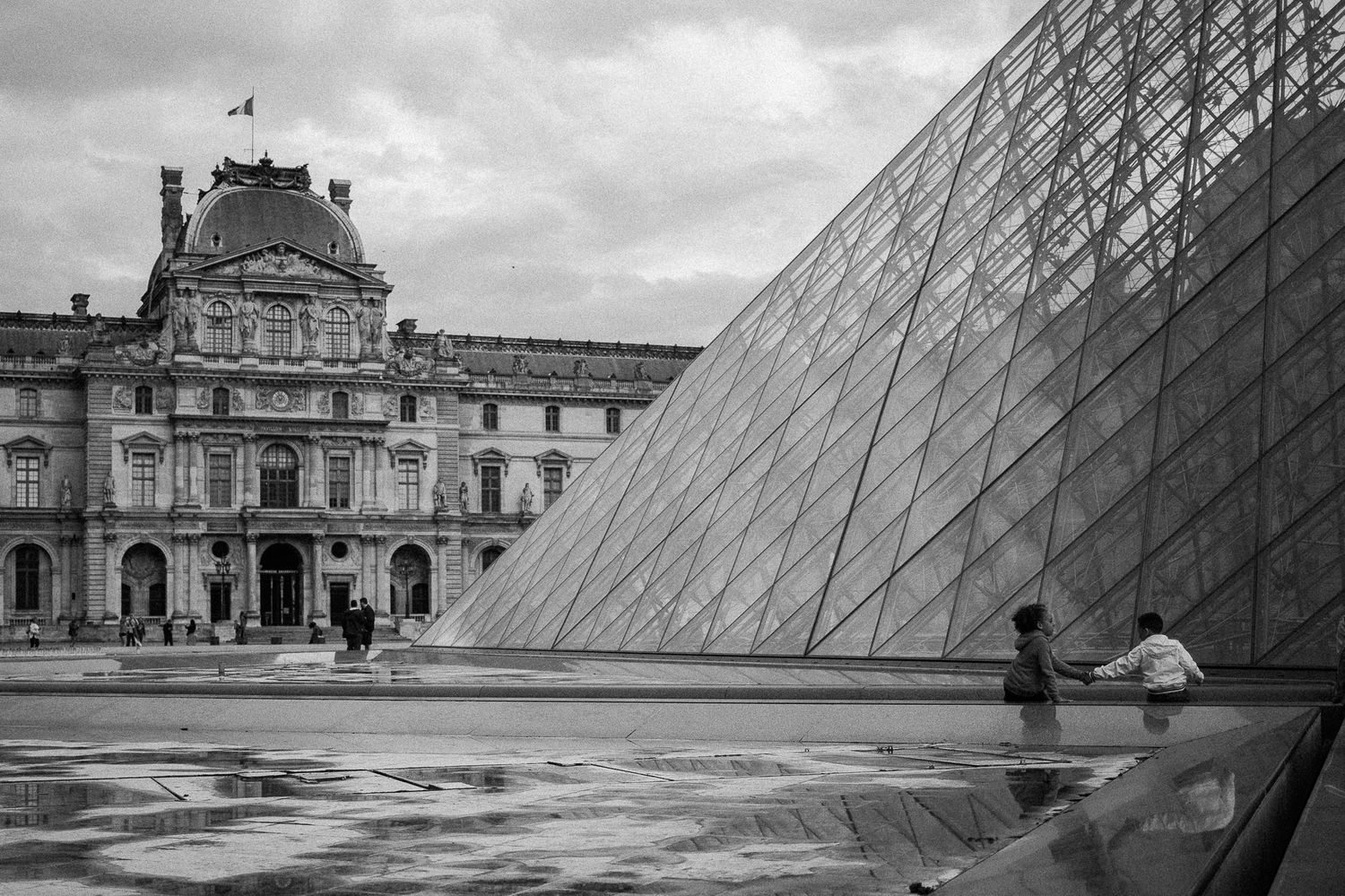 The iconic glass pyramid of the Louvre museum on a cloudy day in Paris.