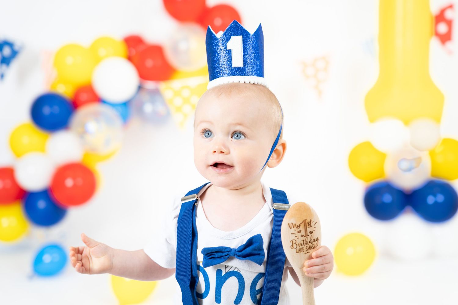 Black and white portrait of baby sitting with birthday decorations in background.