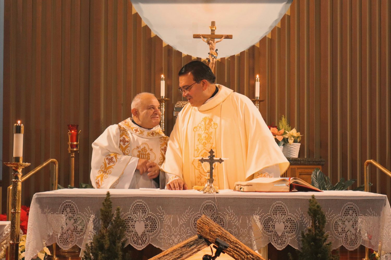 Two clergy members in cream-colored religious vestments stand at an altar during a church ceremony.