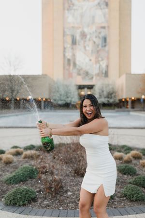 Graduate popping champagne in white dress celebrating at Notre Dame.