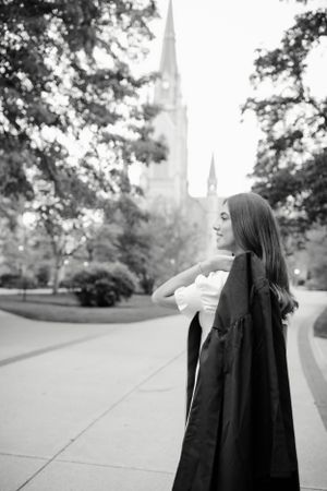Black and white portrait of graduate in academic regalia near campus church spires.