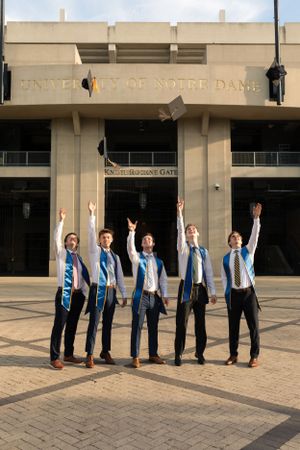 Group celebrating graduation outside Notre Dame stadium entrance with raised arms.