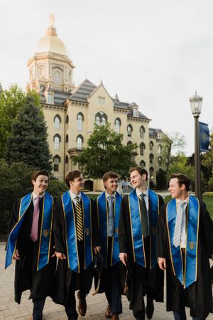 Graduates in blue stoles and black robes pose in front of Notre Dame's iconic Golden Dome building.