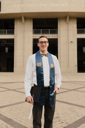 Graduate in academic regalia standing in front of Notre Dame stadium entrance.