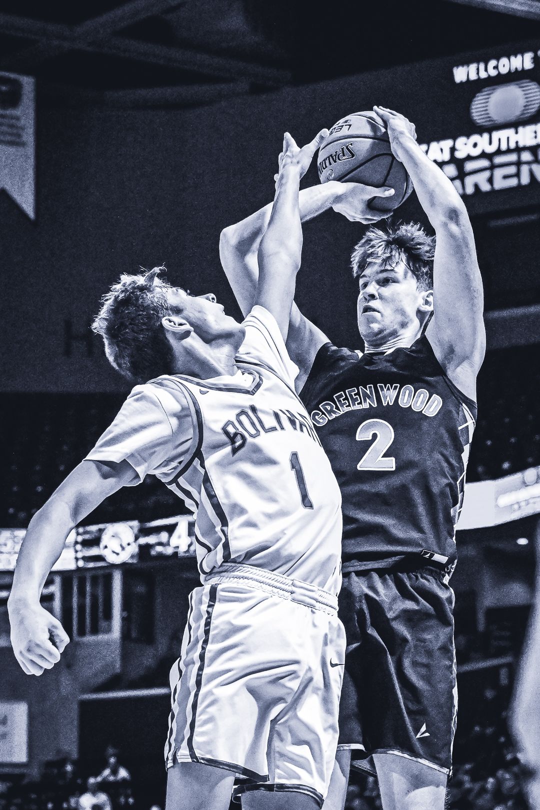 Two basketball players jump high battling for the ball in black and white action shot.