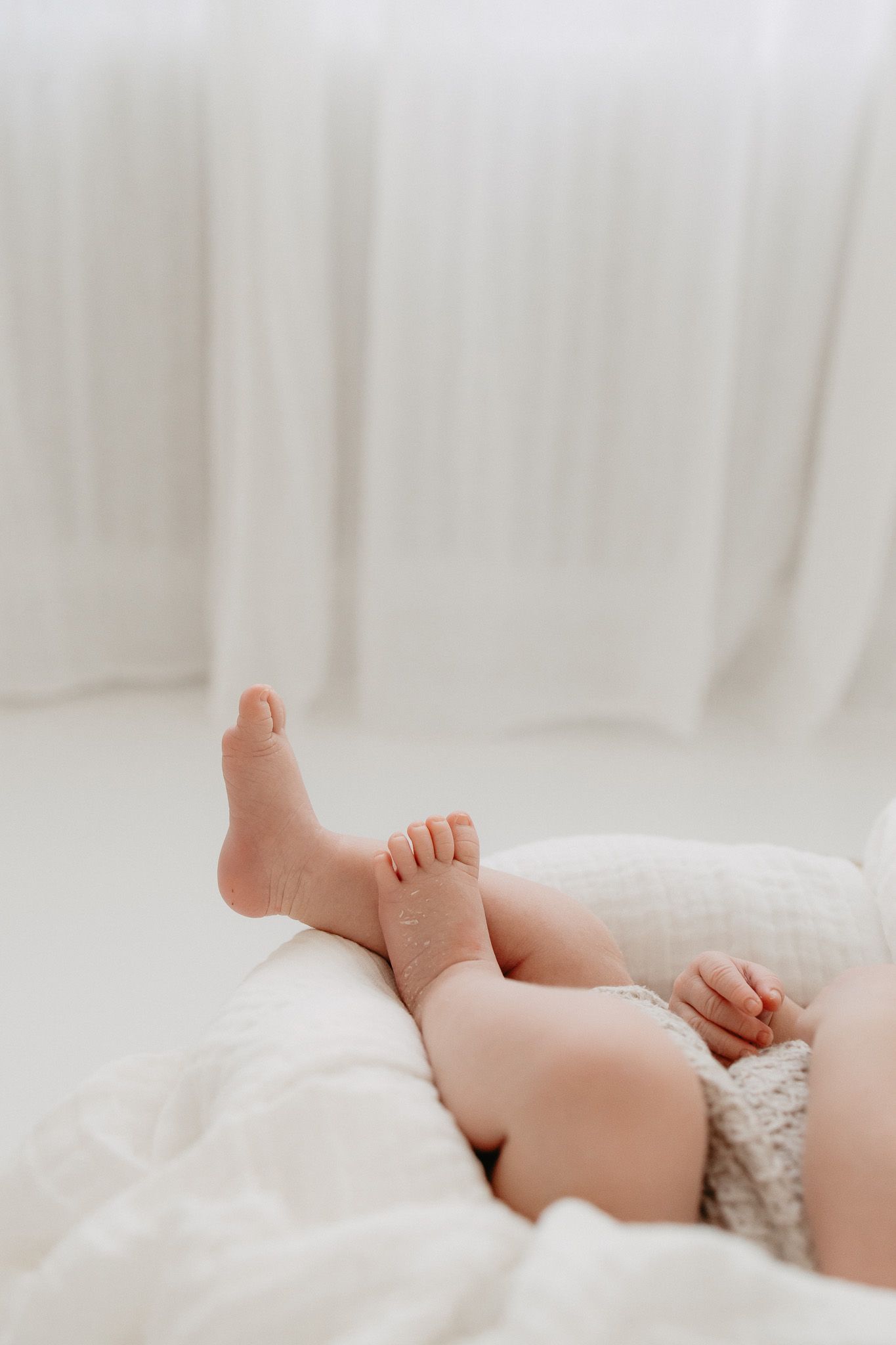 Vauvan pienet jalat lepäävät pehmeällä valkoisella pitsireunuksella varustetulla vuodevaatteella luonnonvalossa. Vastasyntyneen kuvaus