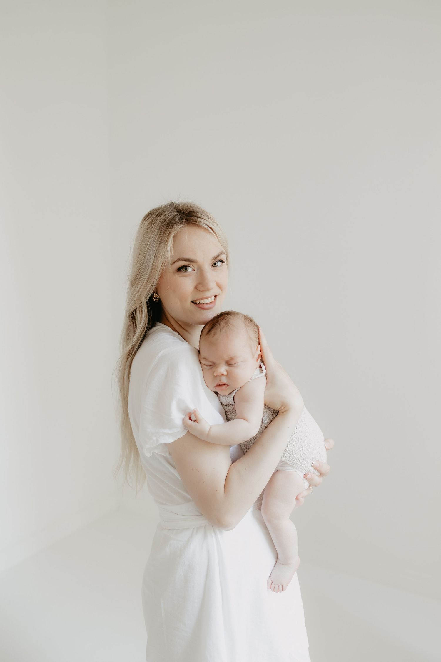 Herkkä hetki tallentui pehmeässä valossa, kun valkoisiin äiti pitelee nukkuvaa. c