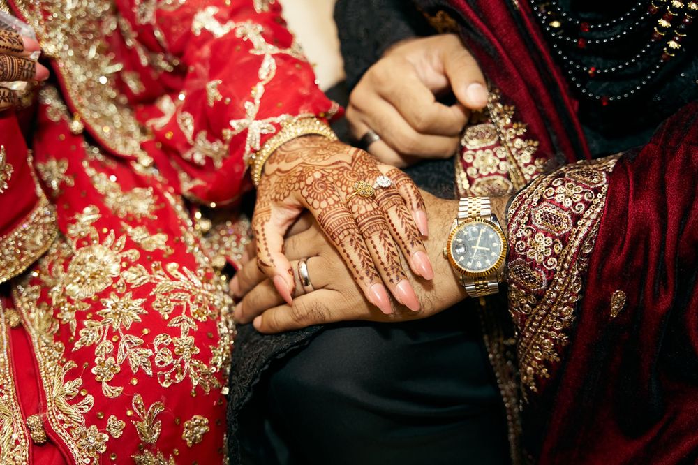 Close-up of intricate henna designs and jewelry on hands at traditional South Asian wedding.