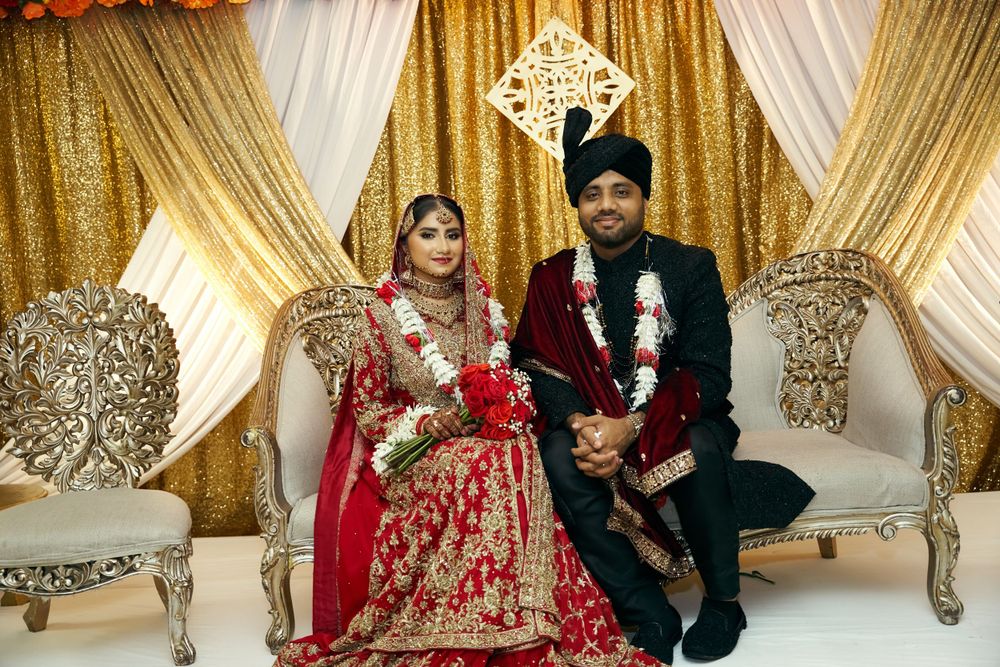 Traditional South Asian wedding couple in ornate red and gold attire on decorated stage.
