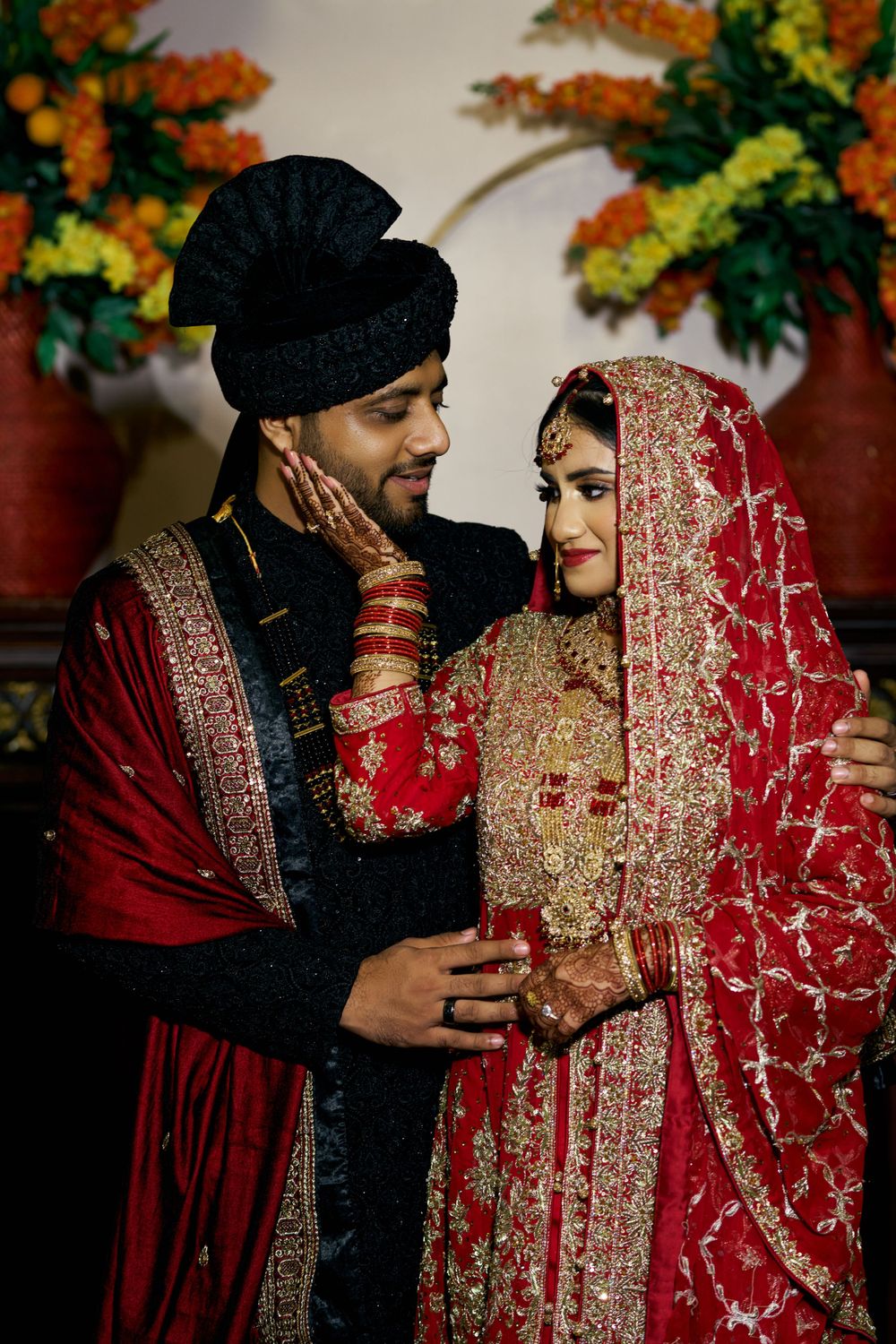 Romantic couple portraits in traditional Indian wedding outfits against colorful floral backdrop.