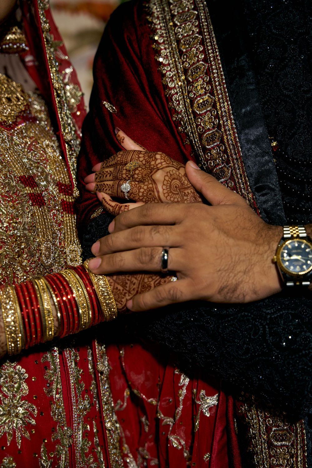 Close-up of hands showing wedding bangles and jewelry against red and gold traditional attire.