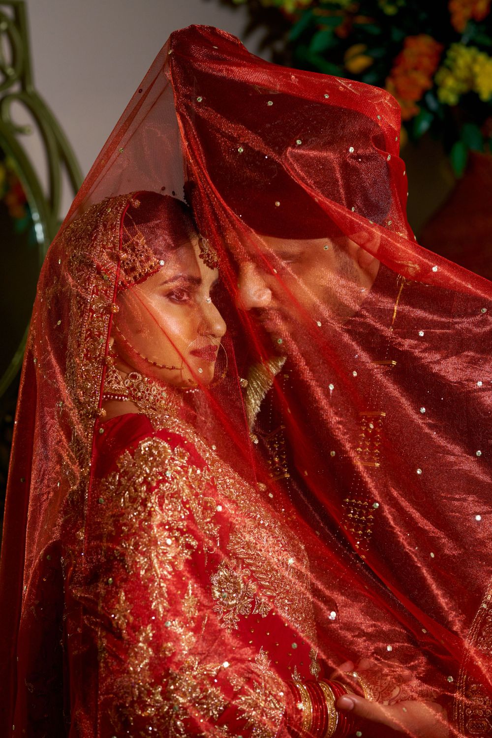 Bride in red dupatta with gold embroidery photographed through translucent veil.