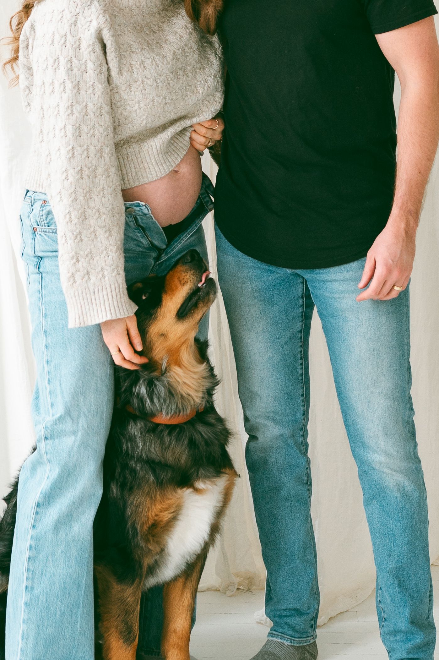 A dog sits between two people wearing jeans and casual clothes against a white background.