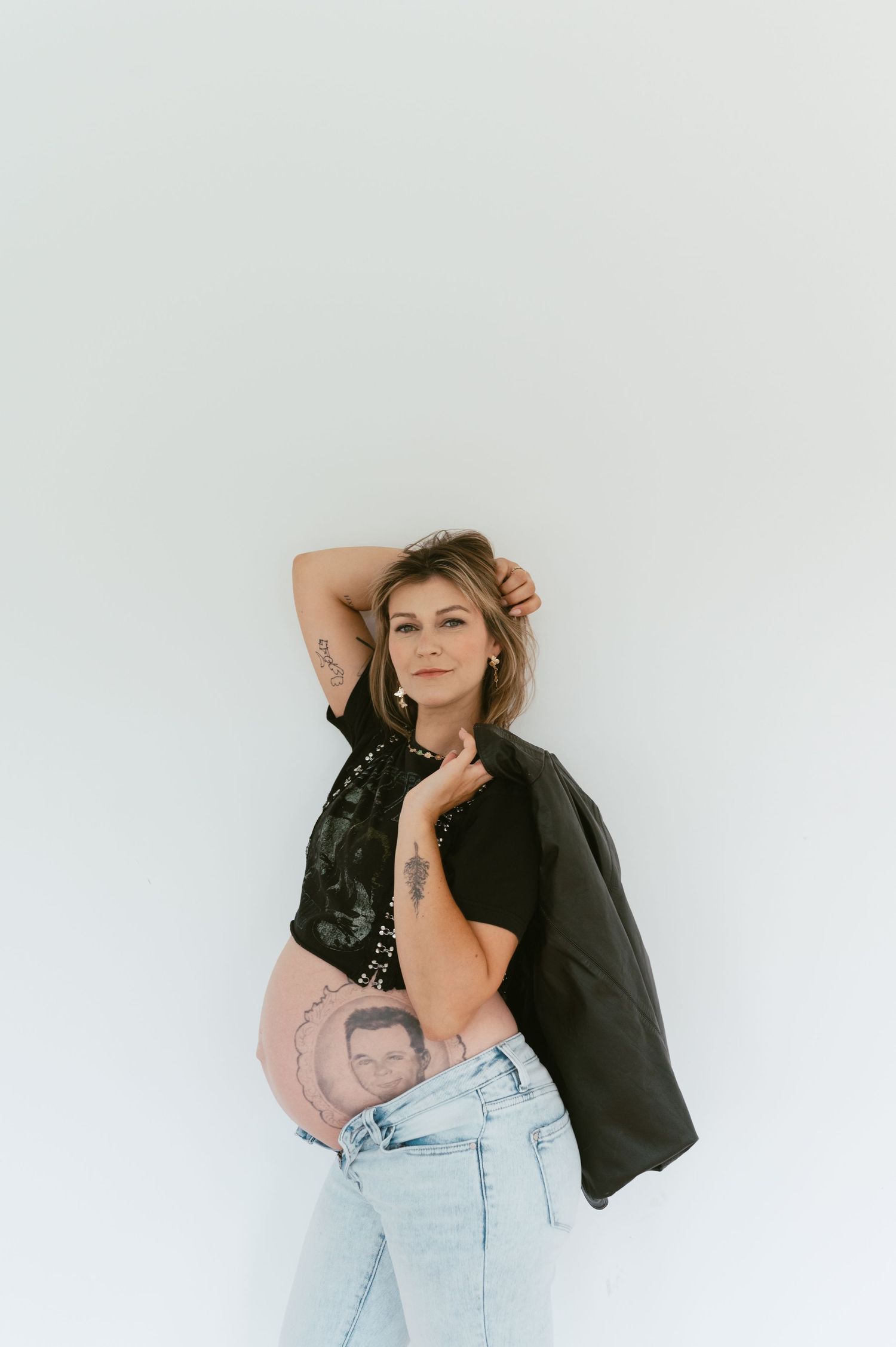 Artistic studio portrait featuring denim, black jacket and creative belly art.