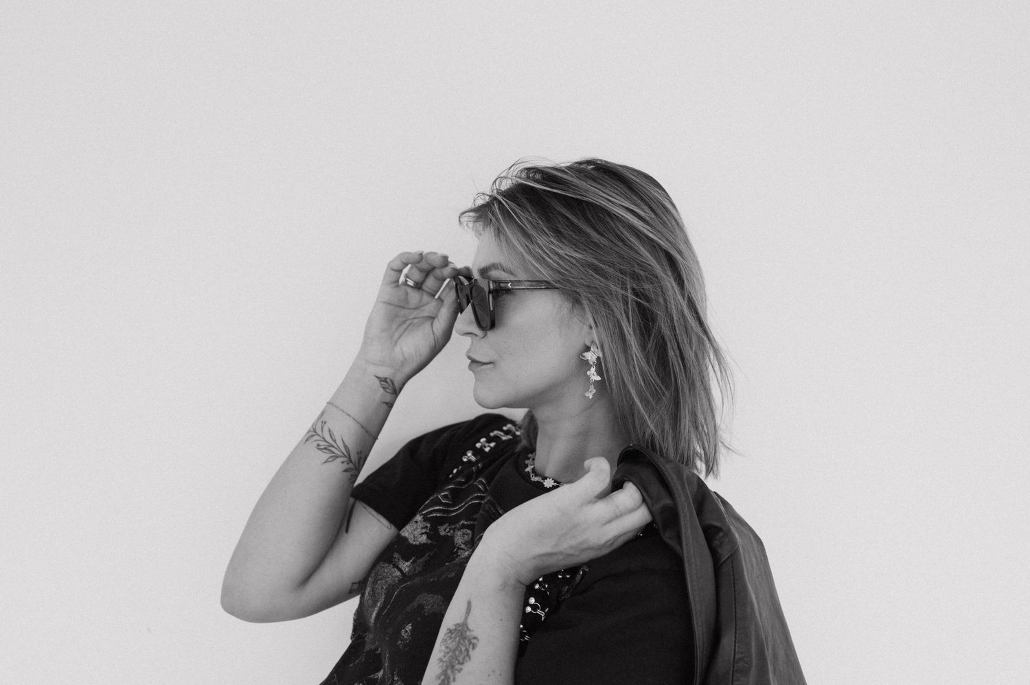 Black and white portrait with sunglasses showing artistic pose against neutral backdrop.