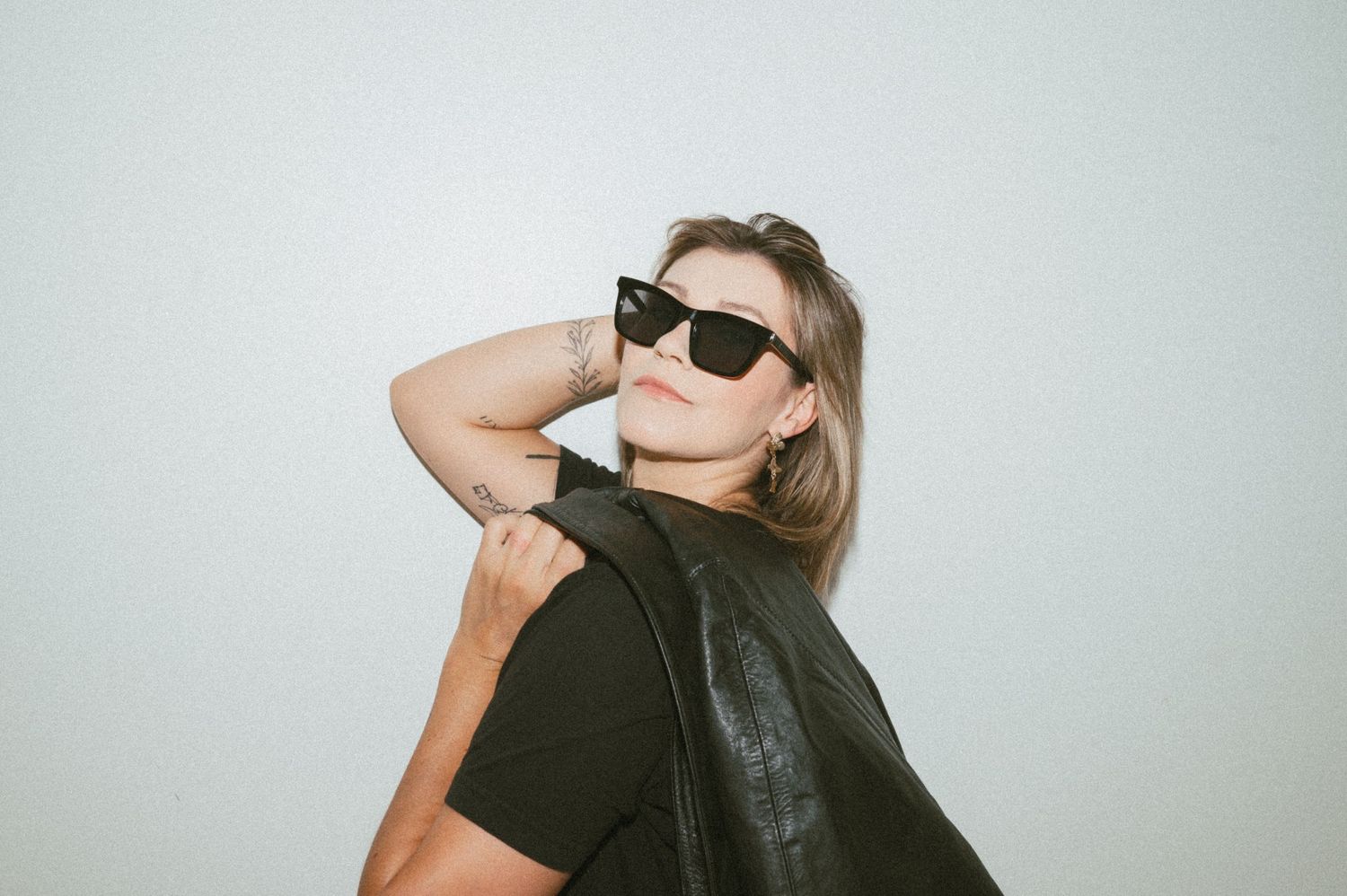 Fashion portrait with sunglasses and black leather jacket against white background.