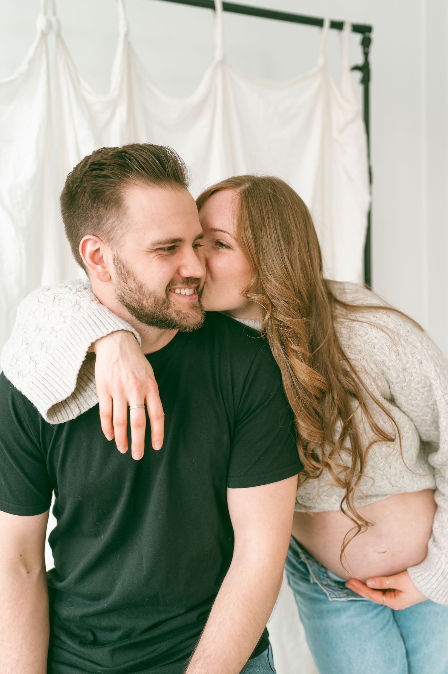 A couple shares an intimate moment together against a white curtain backdrop.