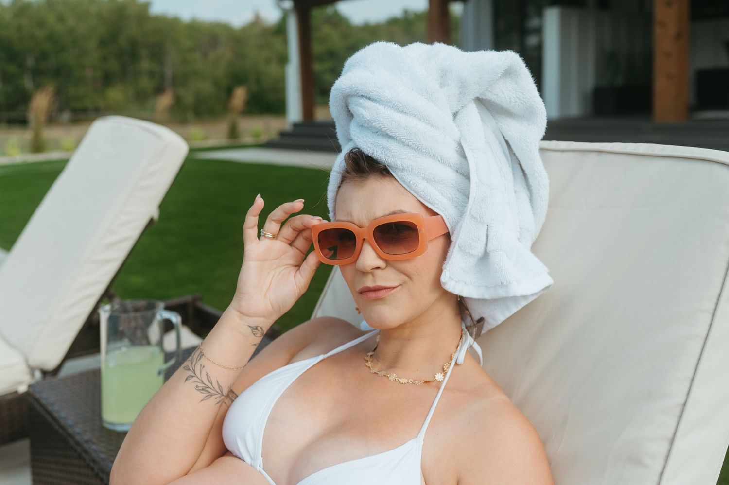 Person in white swimwear and towel turban lounging on chair with sunglasses outdoors.