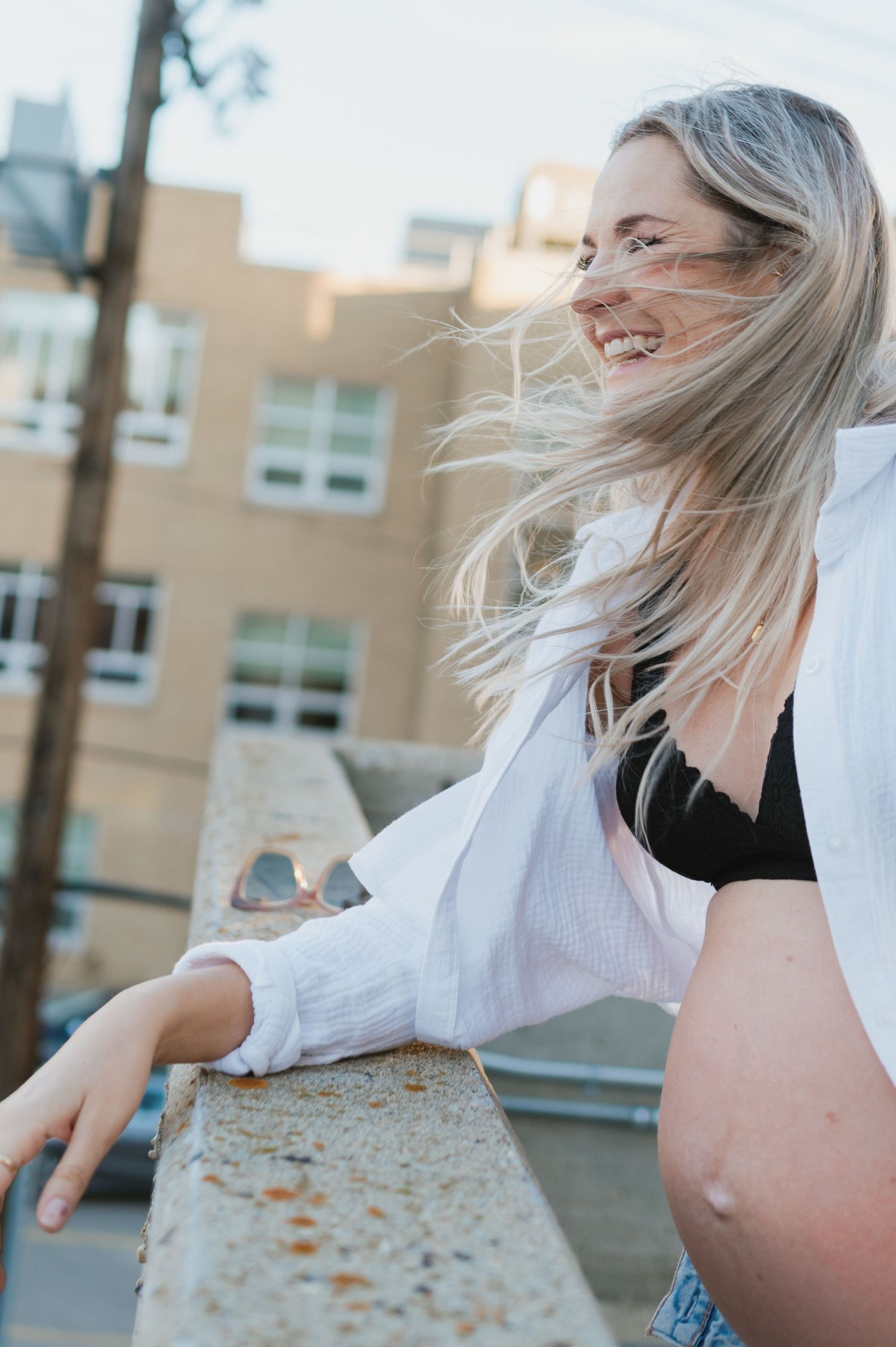 A person with windswept hair poses on an urban rooftop in casual attire.