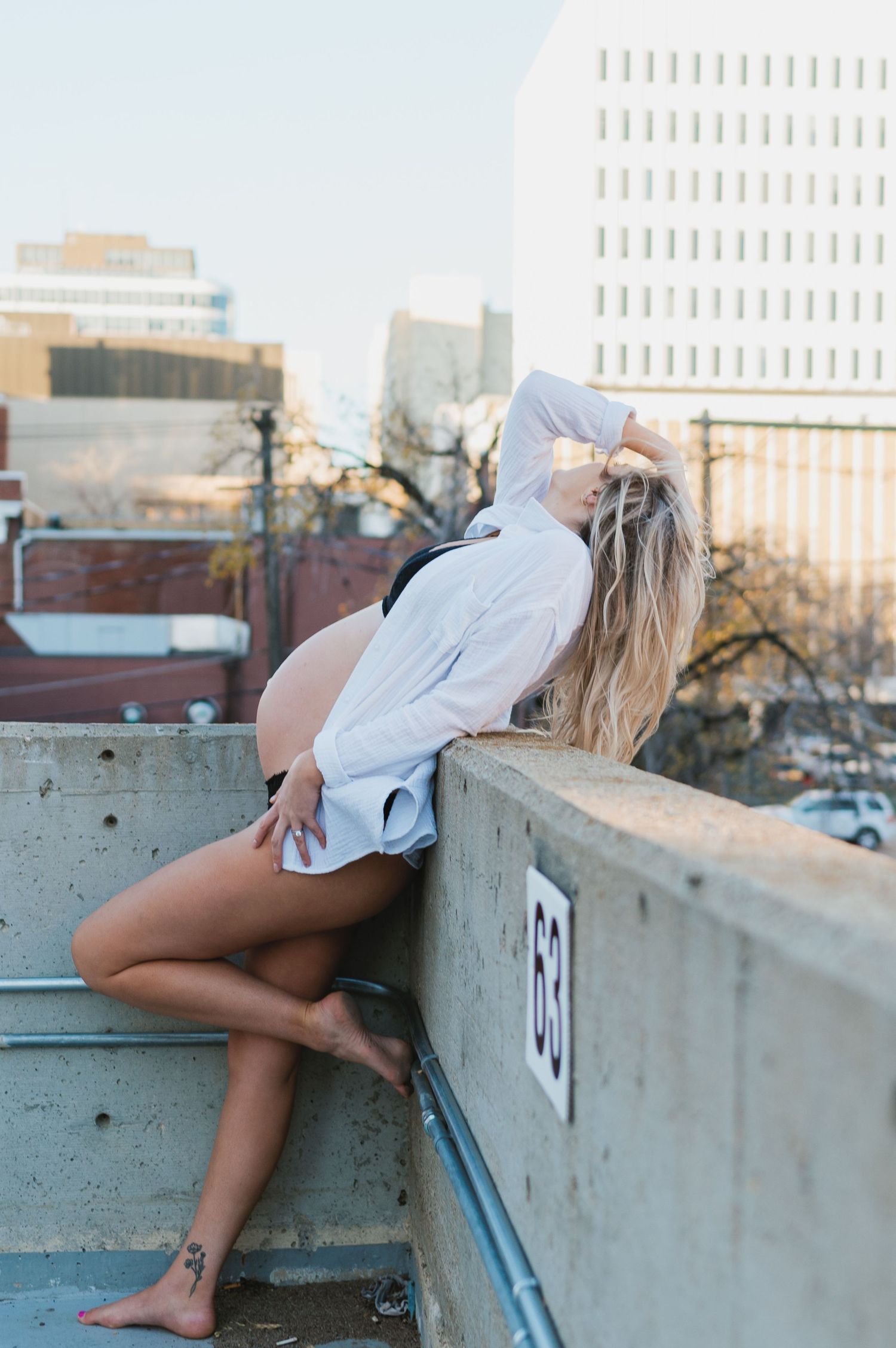 A person in a white shirt poses dramatically on an urban rooftop with cityscape backdrop.