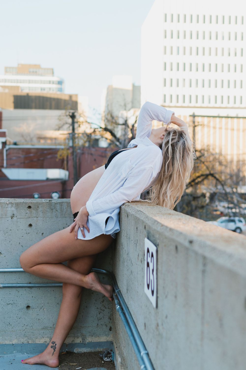 A person in a white shirt poses dramatically on an urban rooftop with cityscape backdrop.
