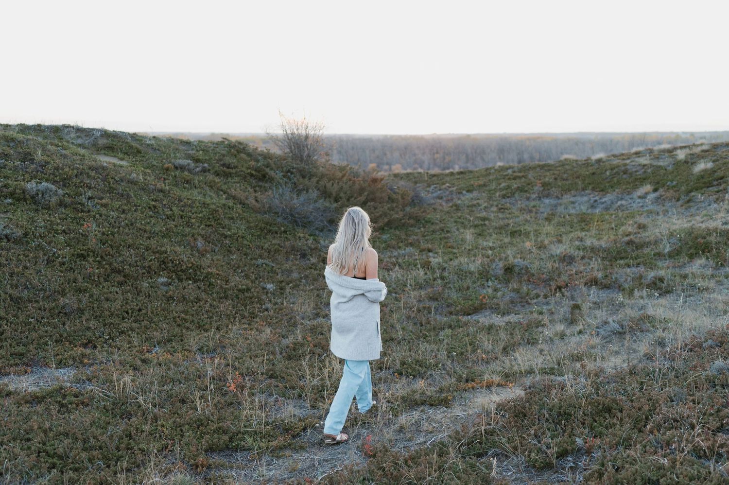 Person in light clothing standing on a hill against a winter landscape.